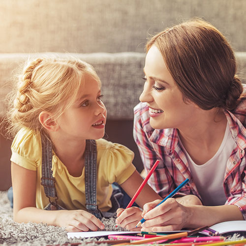 Eine Mutter und ihre Tochter sitzen auf dem Boden und malen mit Buntstiften.