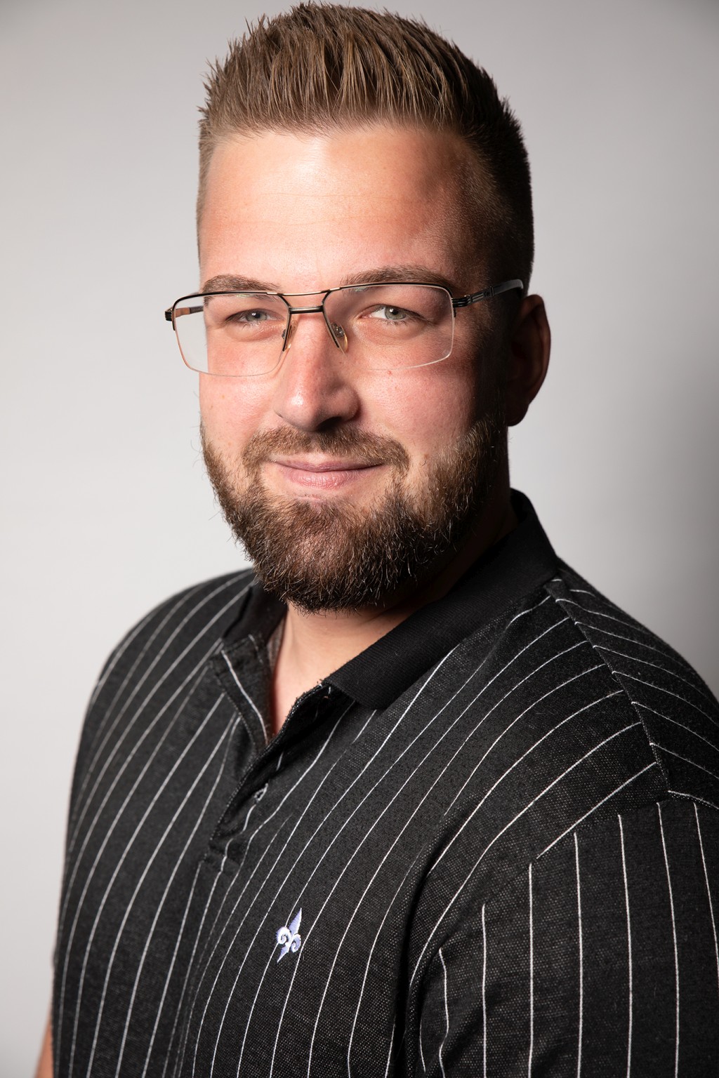 Mann mit Brille und gestreiftem Hemd, der in die Kamera lächelt.