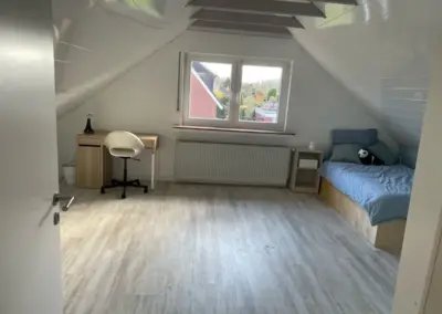 Ein Schlafzimmer mit Dachschräge, einem Bett, einem Schreibtisch und einem Stuhl.