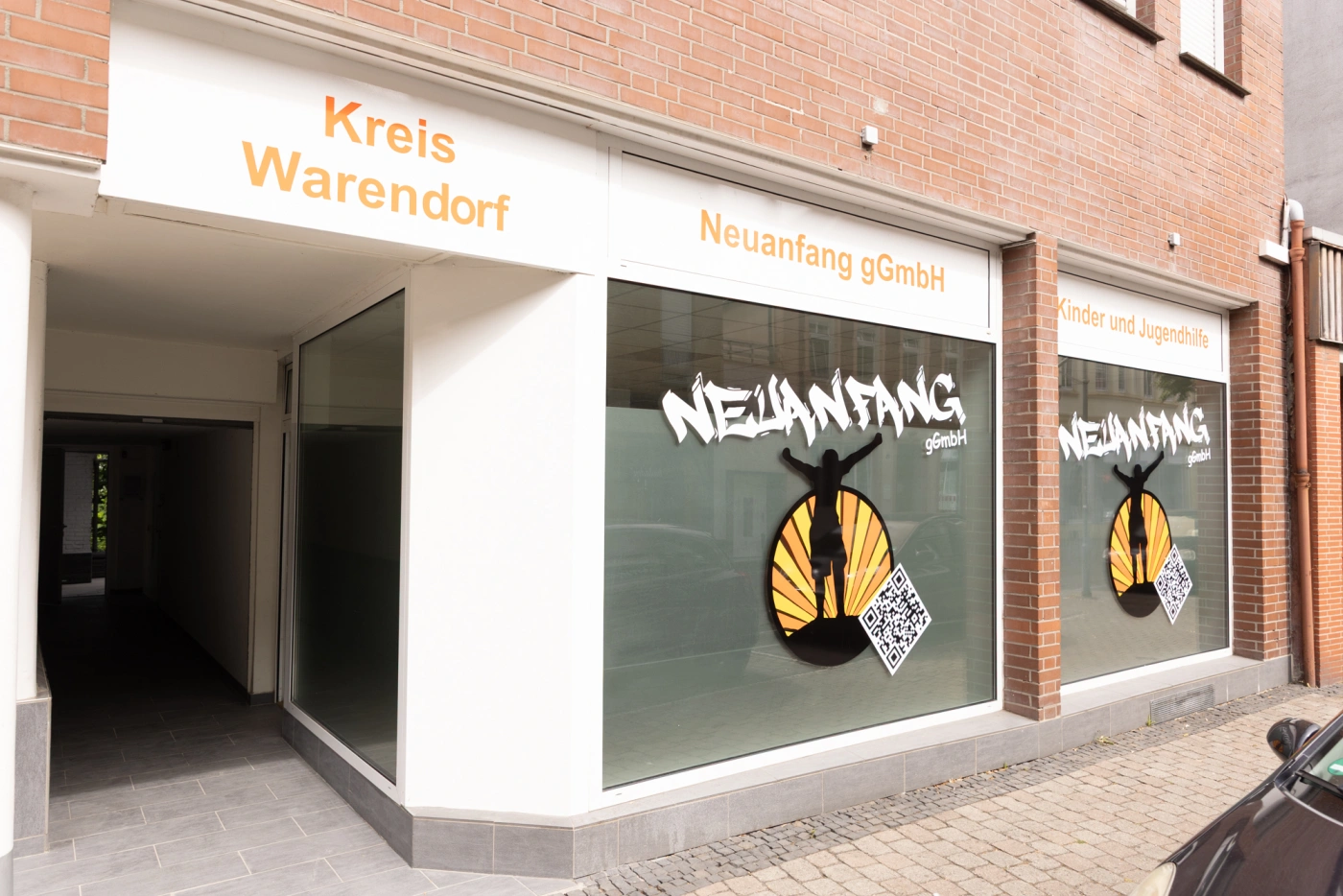 Eingang zur Geschäftsstelle Neuanfang gGmbH mit großen Fenstern und einem auffälligen Logo.