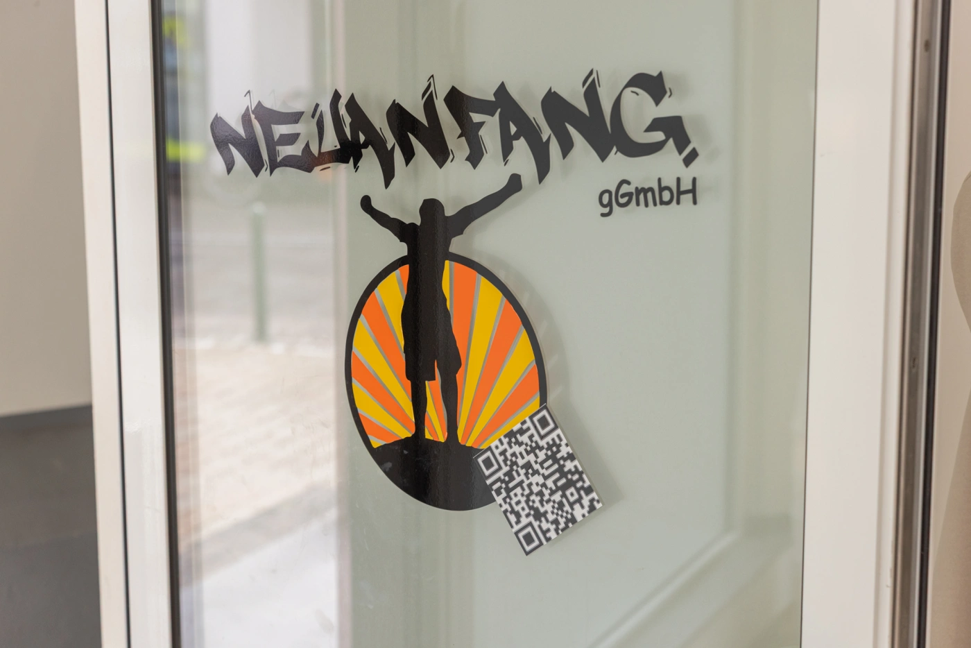 Neuanfang gGmbH Logo mit QR-Code am Glas.