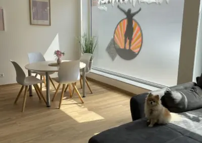 Heller Büroraum im Kreis Warendorf mit Rundtisch, weißen Stühlen, Holzboden und großem Fenster; ein kleiner Hund sitzt auf einer schwarzen Couch.